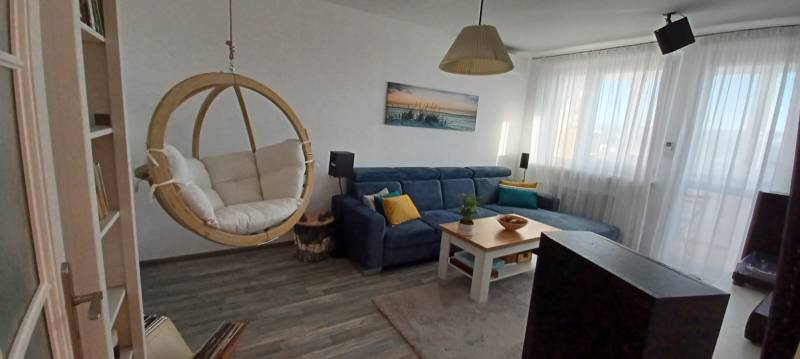 Living room with a swing chair, sofa, and wooden decor flooring, 3-room apartment.