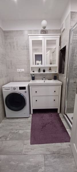 Bathroom with a washing machine, sink, cabinet, and shower in a 3-room apartment.
