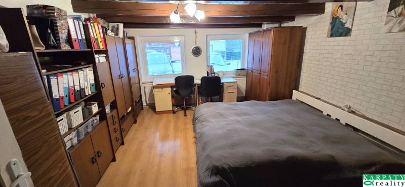 A room in a family house with a wooden decor floor, a bed, and an office corner.