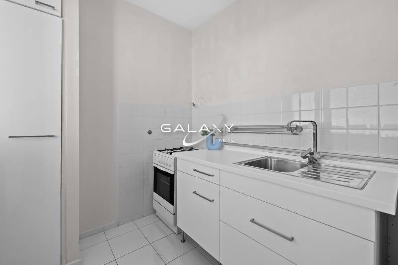 A kitchen in a studio apartment with white kitchen cabinets and a stove.