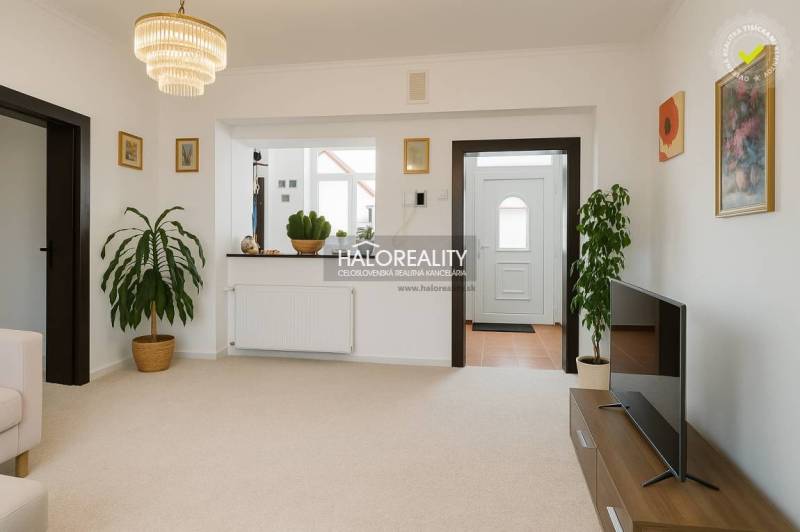 A living room in a family house with white walls, flowers, and a television on a table.