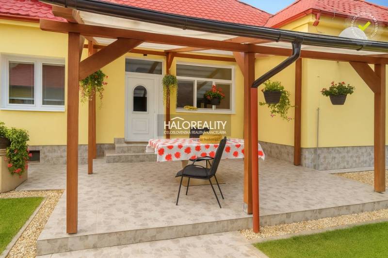 Terrace at a family house in Beša with flowers on a yellow facade and a wooden pergola.