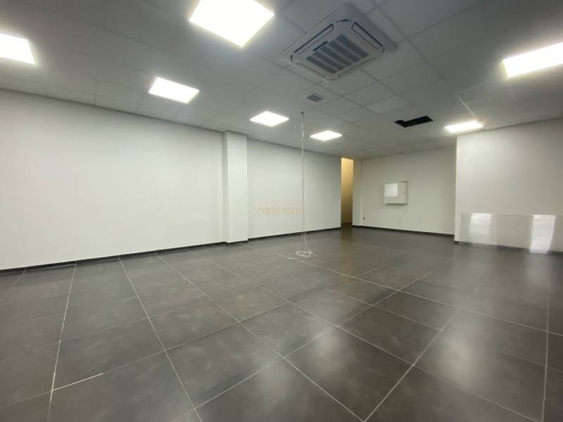 Commercial space with dark flooring and white walls, illuminated by ceiling lights.