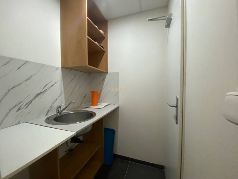 A small kitchenette with a sink, shelves, and an orange pitcher in commercial premises.