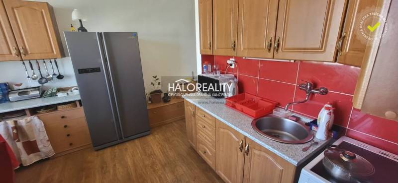 A kitchen in a studio apartment with wooden cabinets, red tiles, and a large refrigerator.