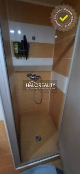 A shower corner in a one-room apartment with orange tiles and wall storage space.