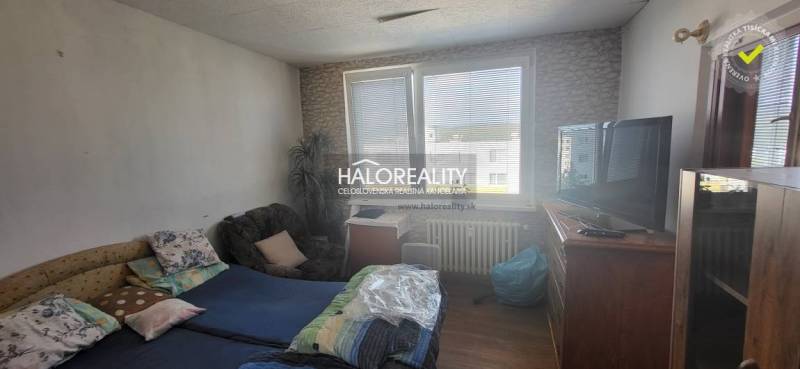 A room in a one-bedroom apartment with a bed, chair, television, and a large window.