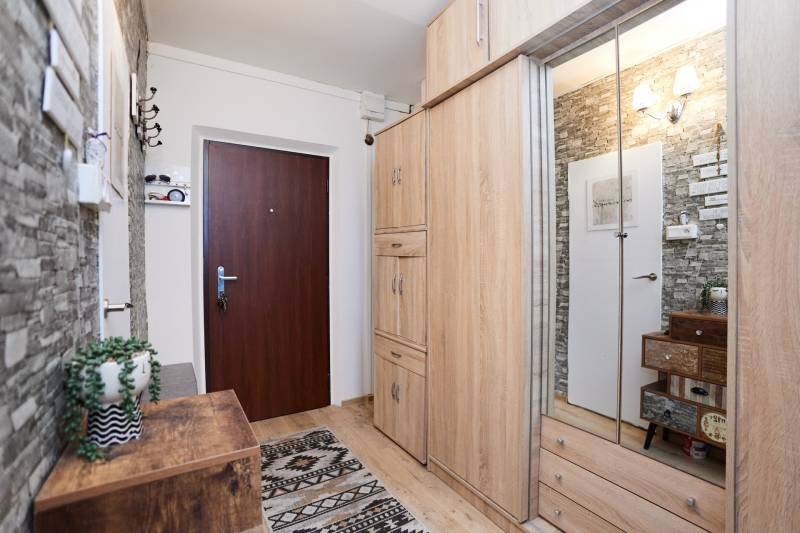 The hallway of a 2-room apartment with a wooden decor floor, stone cladding, and a wardrobe with a mirror.