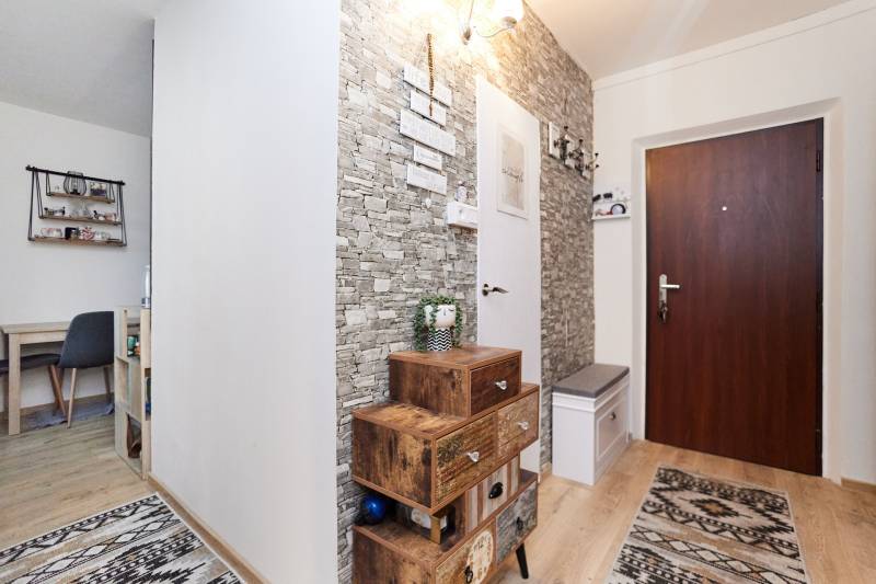 A hallway in a 2-room apartment with decorative stone walls and a floor with a wood decor.