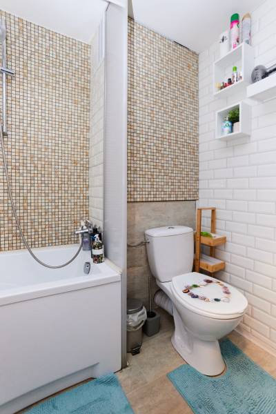 Bathroom with a bathtub, toilet, mosaic on the wall, and shelves for accessories.