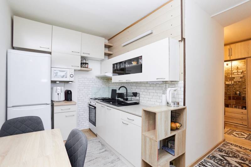 A kitchen in a 2-room apartment with white cabinets and a wooden decor floor.