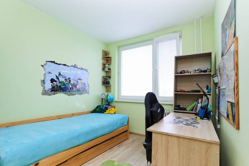 Children's room in a two-room apartment with a bed, a desk, and Minecraft decoration on the wall.