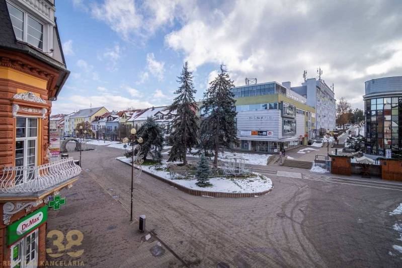 A street in Poprad with commercial buildings, a winter scene, and snow-covered trees.