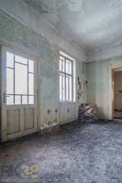 The interior of the building with damaged walls, doors, and windows, bricks on the floor.
