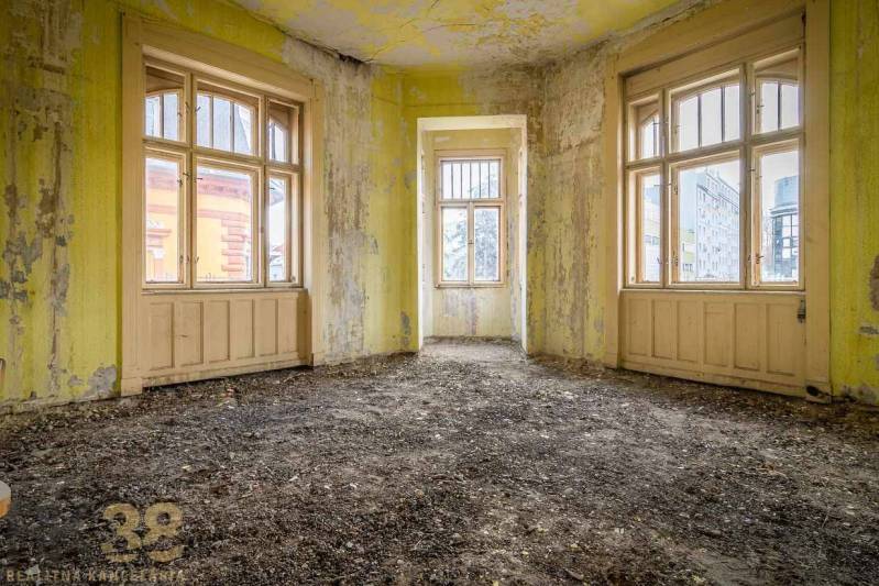 An abandoned room in a building with yellow walls and large windows.