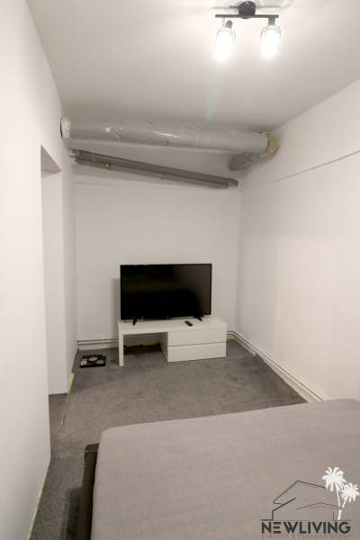 A room in a family house with a television on a white table and a gray carpet.