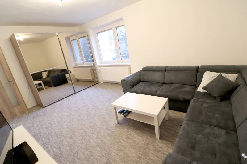 Living room in a family house with a corner sofa, mirrored wardrobe, windows, carpet.