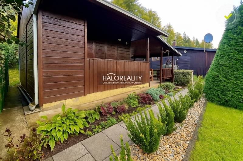 A wooden cottage in the gardens in Bytča, surrounded by well-maintained greenery and a path made of tiles.