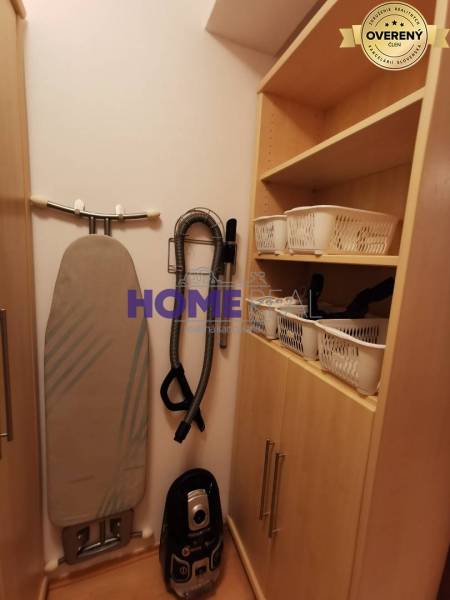 Storage space in a 2-room apartment with a vacuum cleaner and ironing board, wooden cabinets.