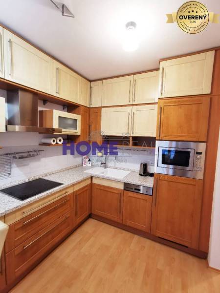 A kitchen in a 2-room apartment with corner-arranged cabinets and a wooden decor floor.