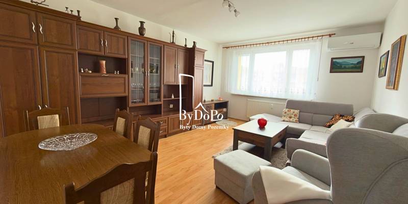 Living room in a three-room apartment with a wooden decor floor and a large sofa set.