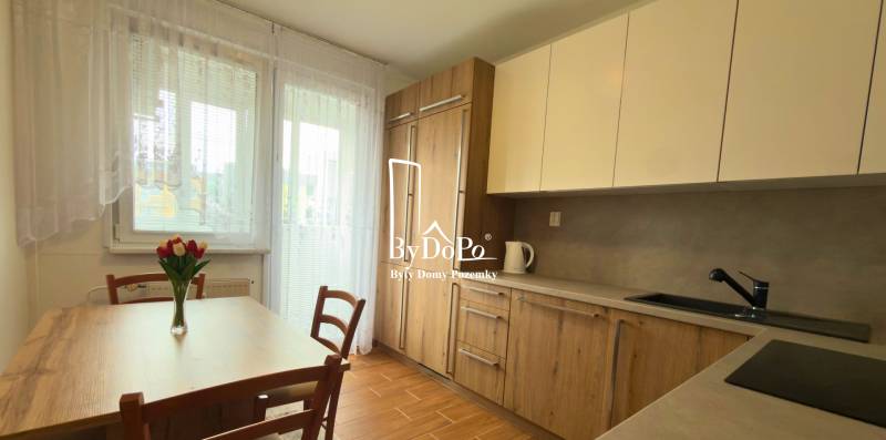 A kitchen in a 3-room apartment with wooden decor and light furniture, elegant flowers on the table.