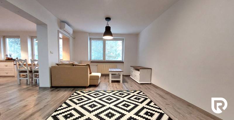 Living room in a 3-room apartment with a sofa, table, wood-patterned floor, and carpet.