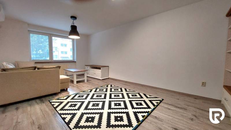 Living room in a three-room apartment with a wooden decor floor and a geometric carpet.