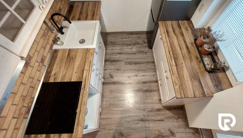 A kitchen in a 3-room apartment with a wooden decor floor and kitchen cabinets.