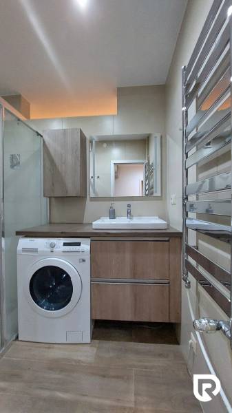 Bathroom with a shower in a 3-room apartment, washing machine and floor with wooden decor.