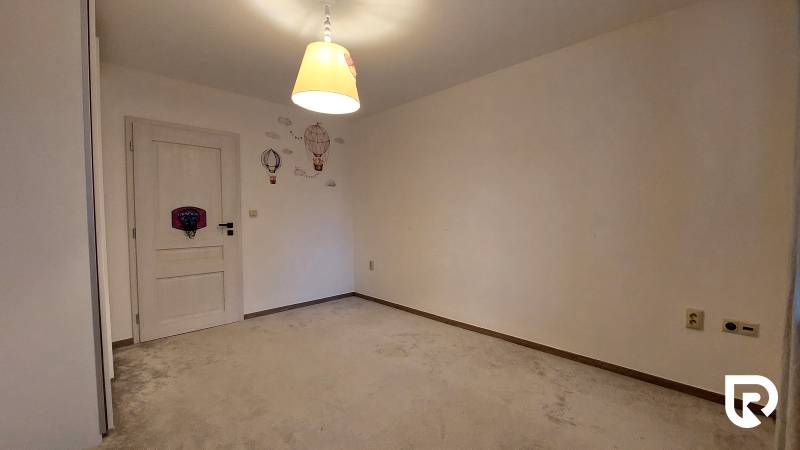 A room in a 3-room apartment with a carpet, a bright lamp, and wall decorations.