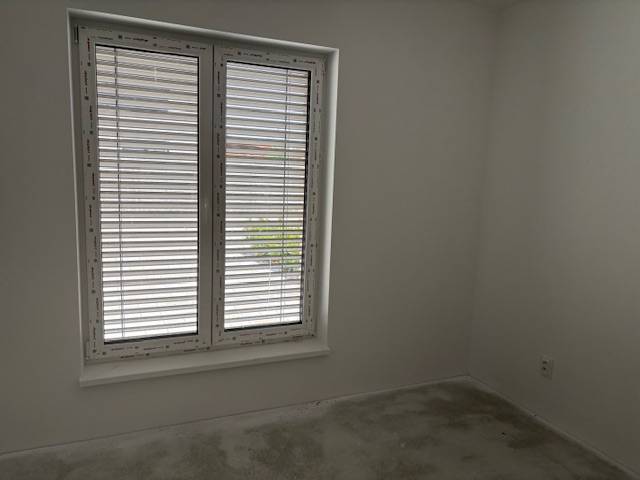 A room in a family house with a large window and blinds, white walls, gray floor.