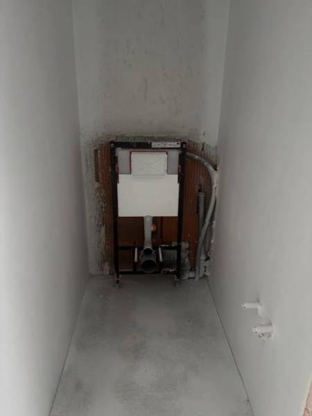 Installation for a wall-hung toilet in the bathroom of a family house. The walls and floor are unfinished.