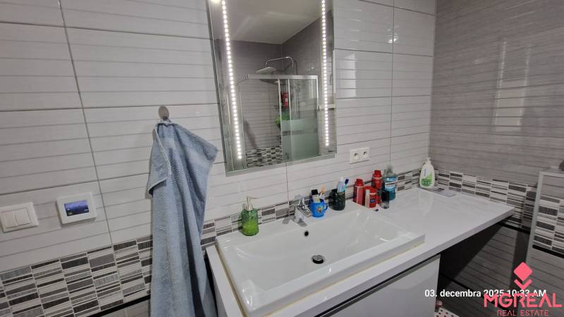 Bathroom in a family house with a sink, mirror with lighting, and a shower enclosure.
