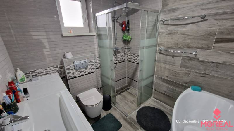Bathroom in a family house with a toilet, shower, and bathtub, floor with wooden decor.