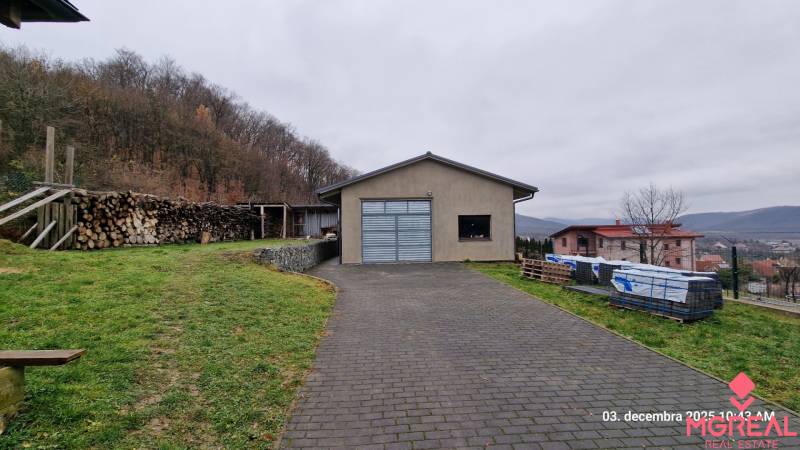 A family house on Kopaninova Street in Sokolie surrounded by nature, a pile of wood, and a driveway.