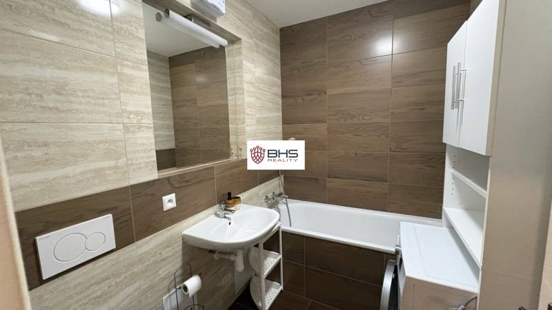Bathroom in a studio apartment with a bathtub and a washing machine, tiles with a wood decor.