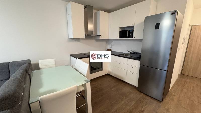 A kitchen unit in a one-room apartment with a wood-patterned floor and a dining table.