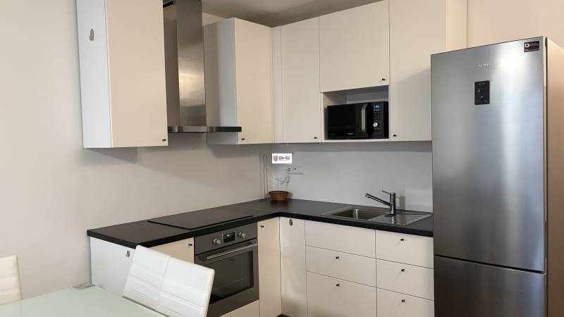 A kitchen in a studio apartment with built-in appliances, white cabinets, and a stainless steel refrigerator.