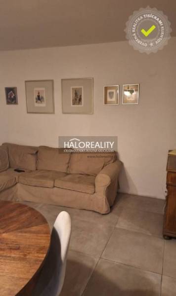 Living room in a three-room apartment with a sofa, wooden decor flooring, and decorative paintings.