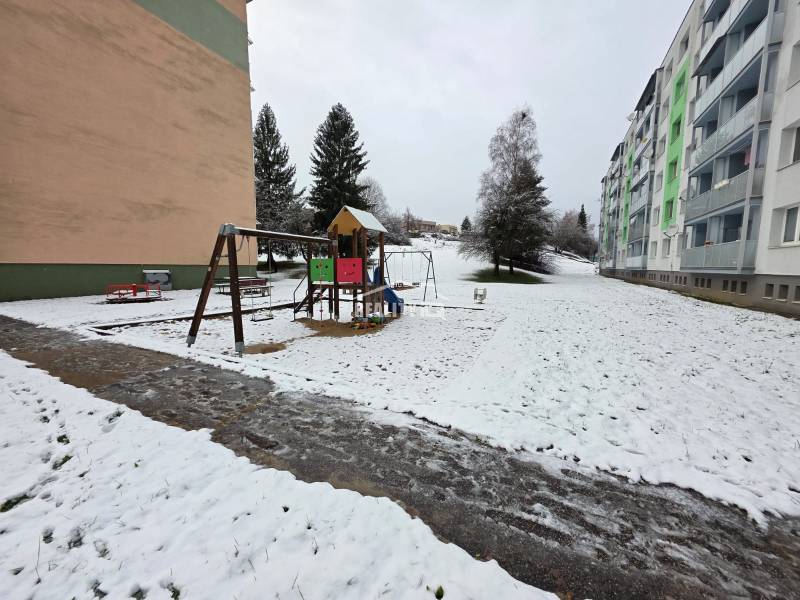 Children are playing in a snowy playground in front of apartment buildings in Považská Bystrica, 4-room apartment.
