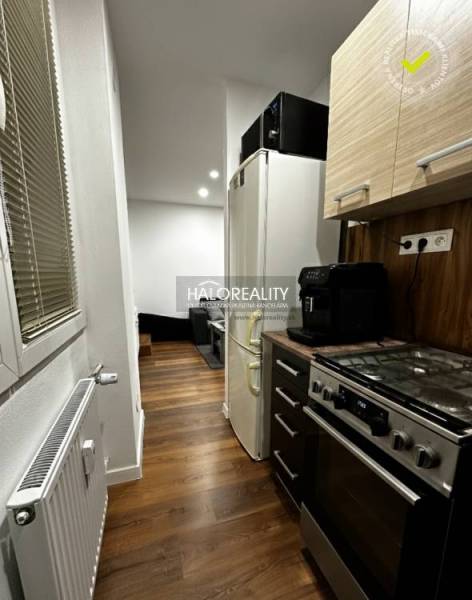 A kitchen in a studio apartment with a wood-patterned floor, a stove, and a refrigerator.