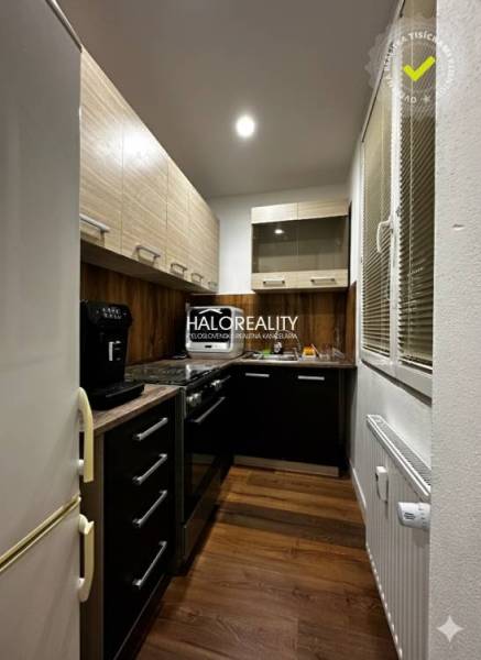 A kitchen in a one-room apartment with a wood-patterned floor and dark cabinets.