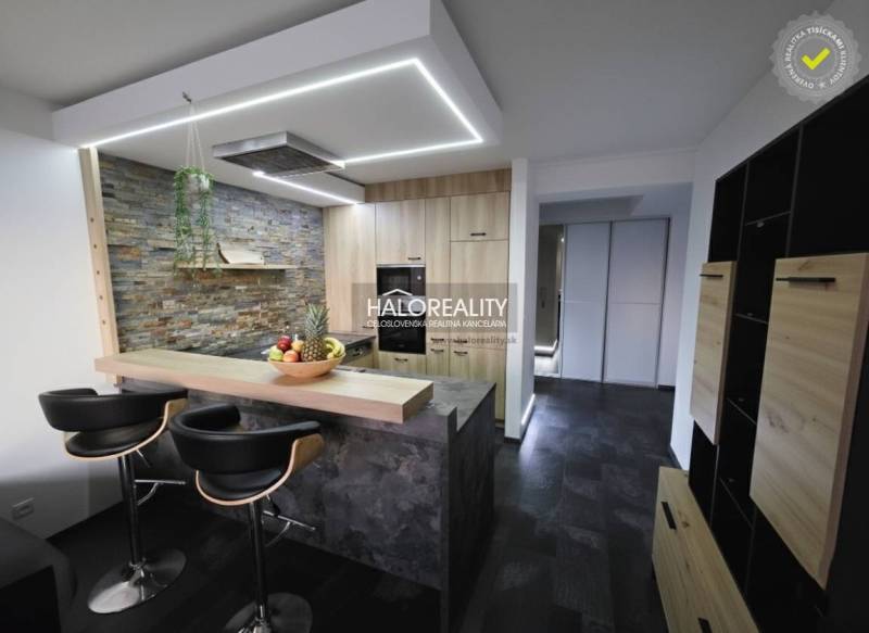 A kitchen in a 2-room apartment with a bar counter, stone cladding, and dark flooring.