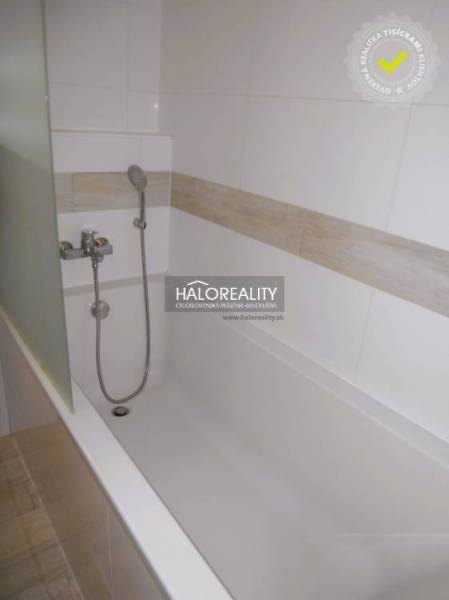 A bathtub in the bathroom of a 2-room apartment with ceramic tiles and a showerhead.