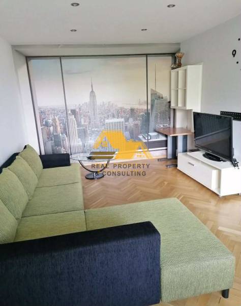 Living room with a sponge cake-colored couch, New York wallpaper, and a wood-patterned floor in a 3-room apartment.