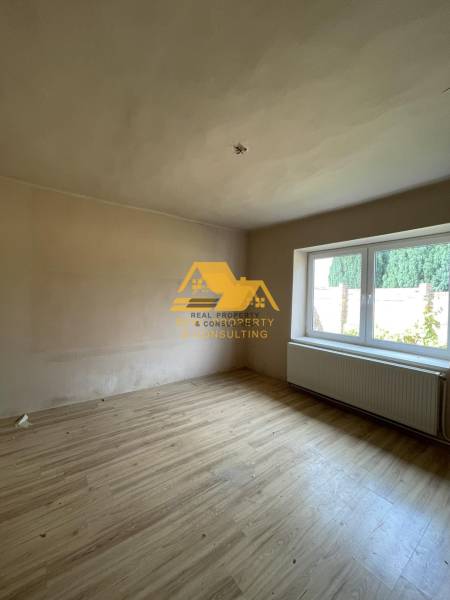 A room with a wooden decor floor and a large window in a family house.