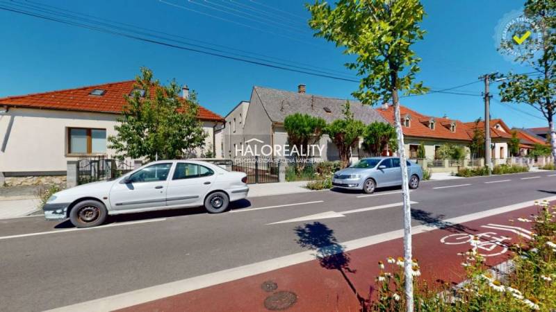 A street in Malacky with family houses, parked cars, and a bicycle lane.