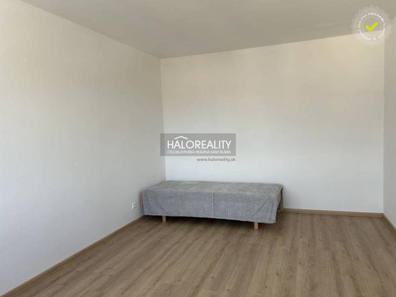 A simple room in a studio apartment with a bed and a wooden-patterned floor.