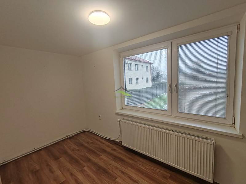 A room in a 3-room apartment with a wooden decor floor and a large window with a view.